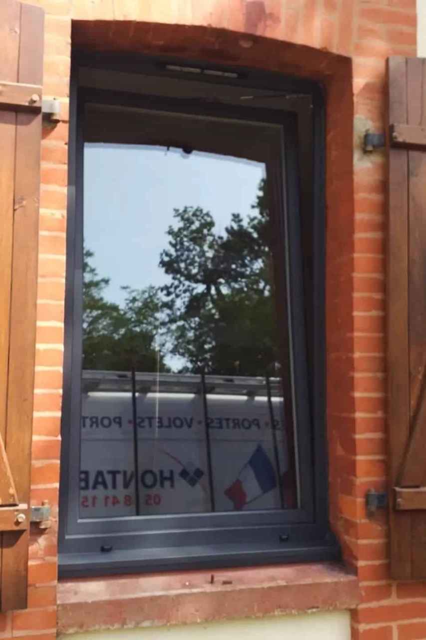 Fenêtre aluminium anthracite posée en rénovation, encadrement brique et volets bois