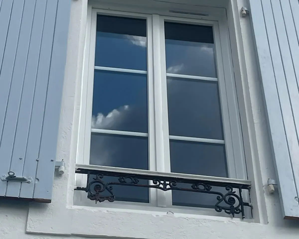 Fenêtre blanche avec volets bleus et balcon en fer