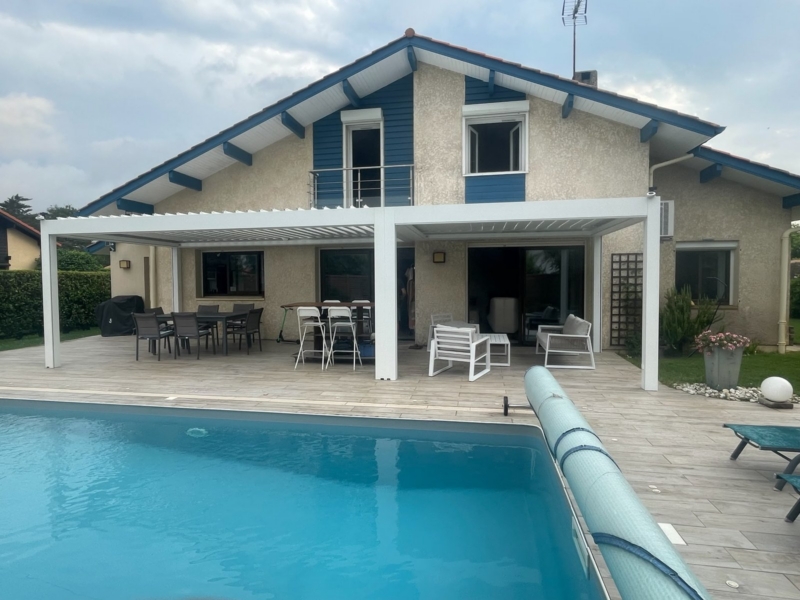 Pergola bioclimatique blanche à deux modules adossée à la façade d'une maison avec piscine dans les Landes, installée par Hontabal