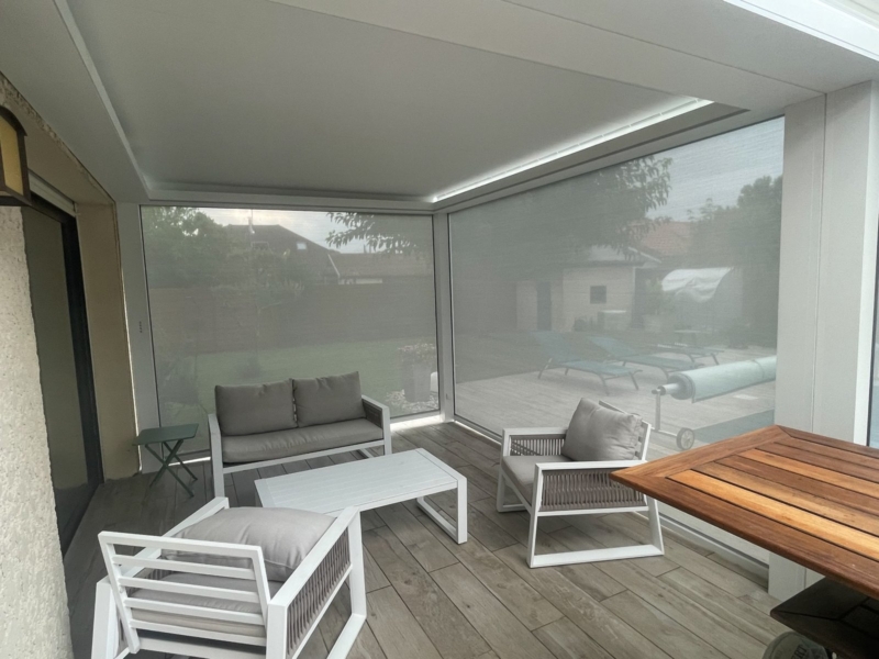 Intérieur d'une pergola bioclimatique fermée par ses stores screen, salon de jardin protégé du vent et du soleil