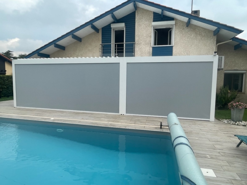 Stores screen latéraux descendus sur une pergola bioclimatique au bord d'une piscine dans les Landes