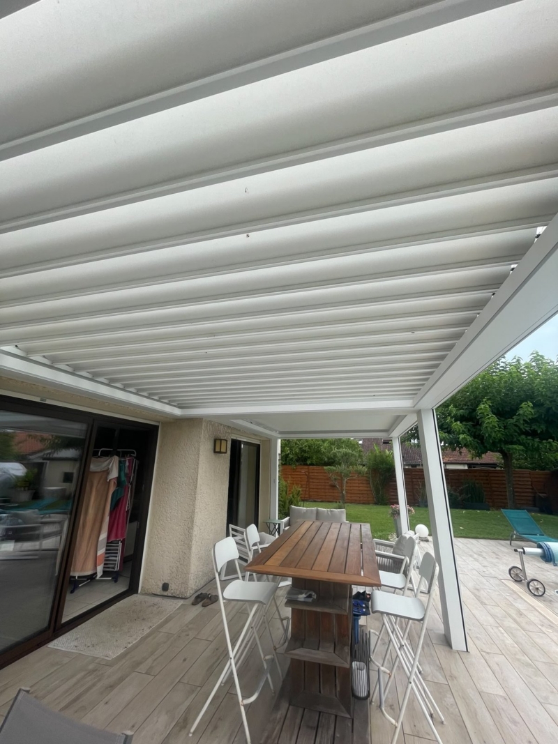 Lames de toiture ouvertes et structure aluminium blanche d'une pergola bioclimatique vues depuis la terrasse