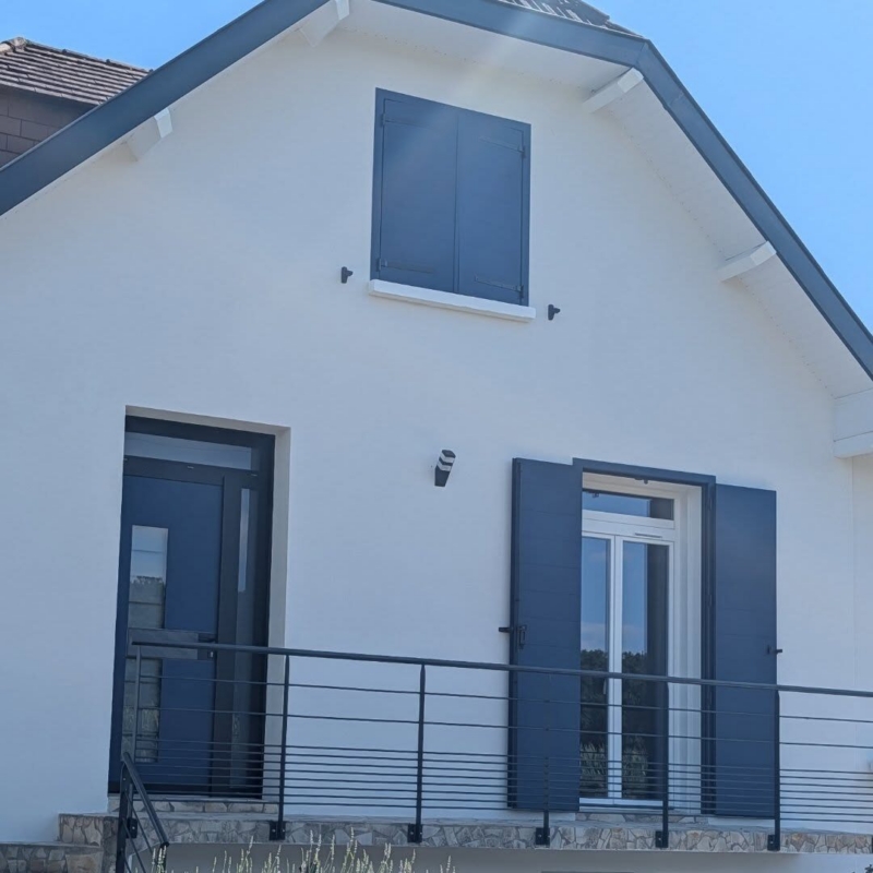 Pignon de la maison avec porte d'entrée bleue, porte-fenêtre PVC sur balcon et volets battants aluminium assortis