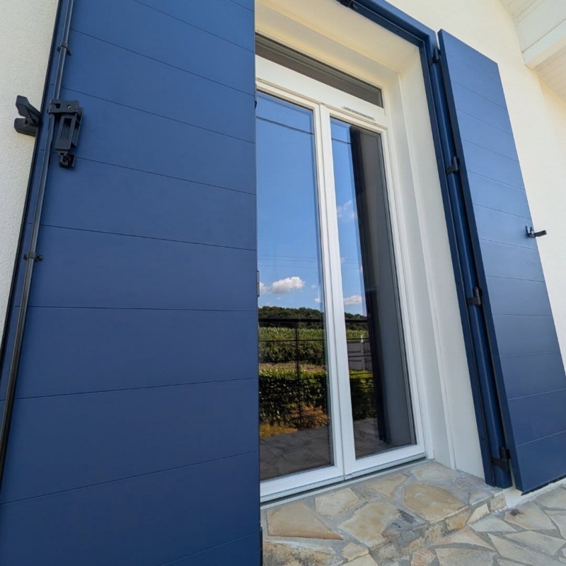 Détail d'un volet battant aluminium Cécilia bleu sur précadre devant une porte-fenêtre PVC OuvertureS ReferenS