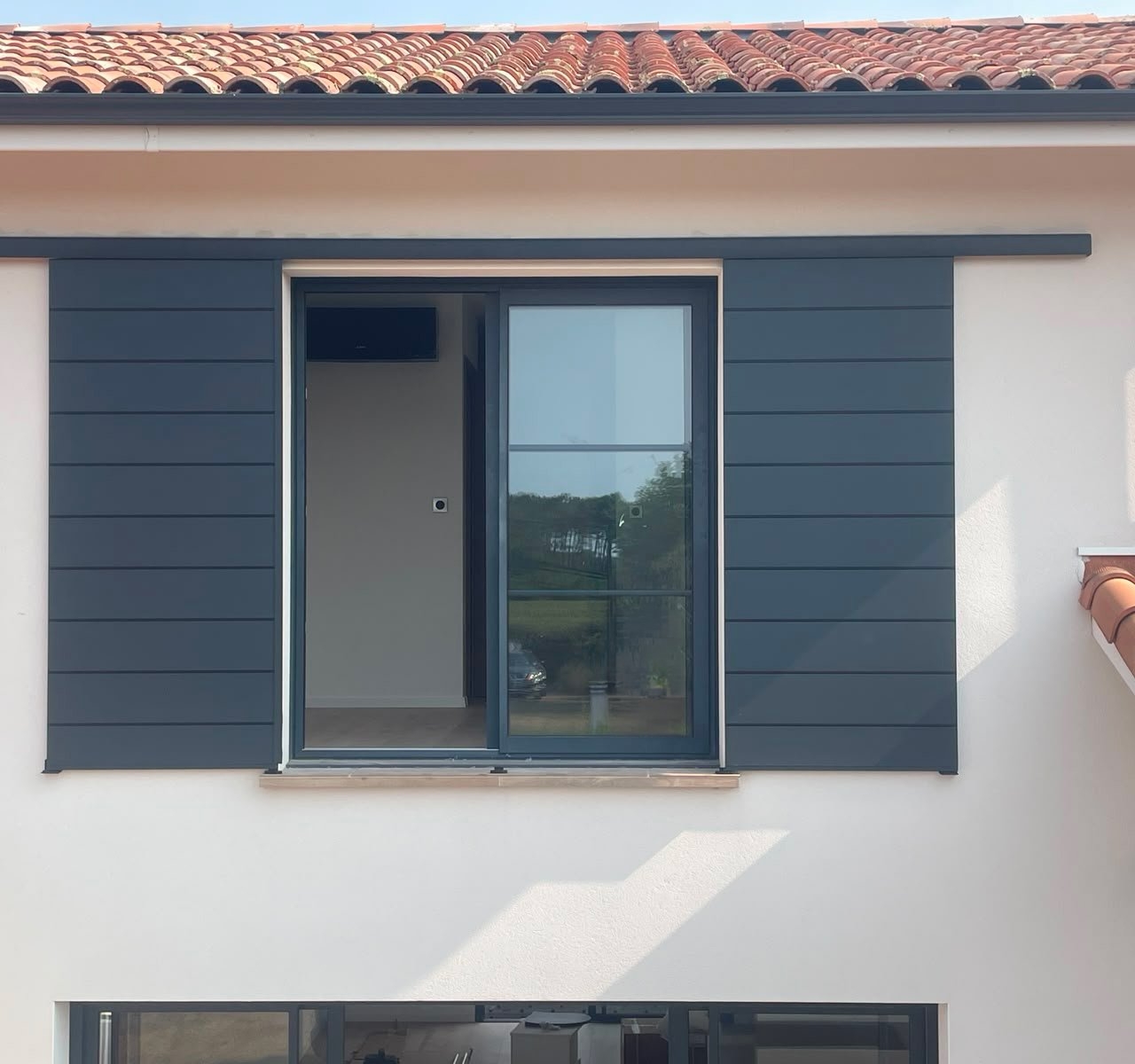 Volet coulissant ouvert, vantaux rangés de chaque côté d'une fenêtre coulissante en aluminium gris, maison contemporaine à Mimizan