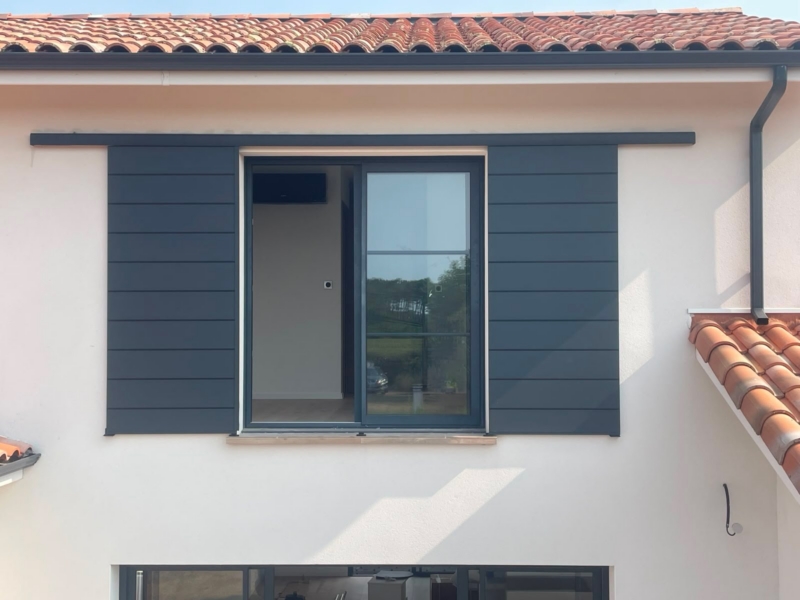 Volet coulissant ouvert, vantaux rangés de chaque côté d'une fenêtre coulissante en aluminium gris, maison contemporaine à Mimizan