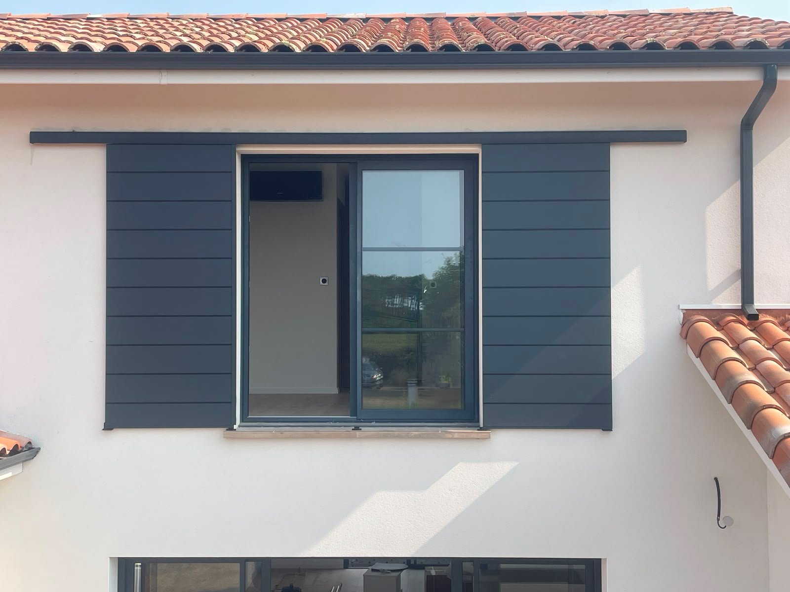 Volet coulissant ouvert, vantaux rangés de chaque côté d'une fenêtre coulissante en aluminium gris, maison contemporaine à Mimizan
