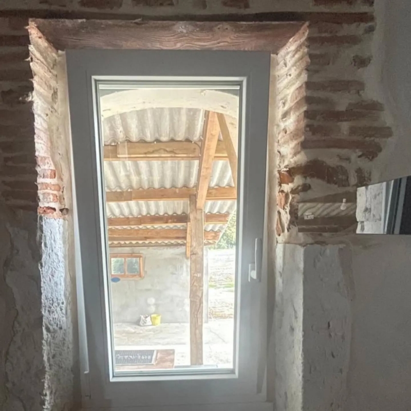 Fenêtre PVC dans une ouverture en briques avec linteau en bois, bâti traditionnel à Misson