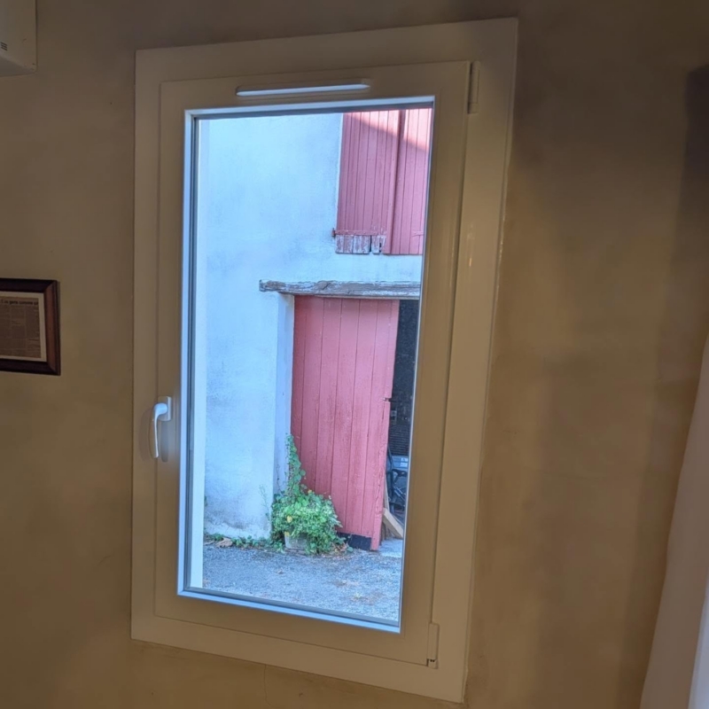 Fenêtre PVC blanche avec entrée d'air dans un mur enduit, rénovation d'un bâti ancien à Misson