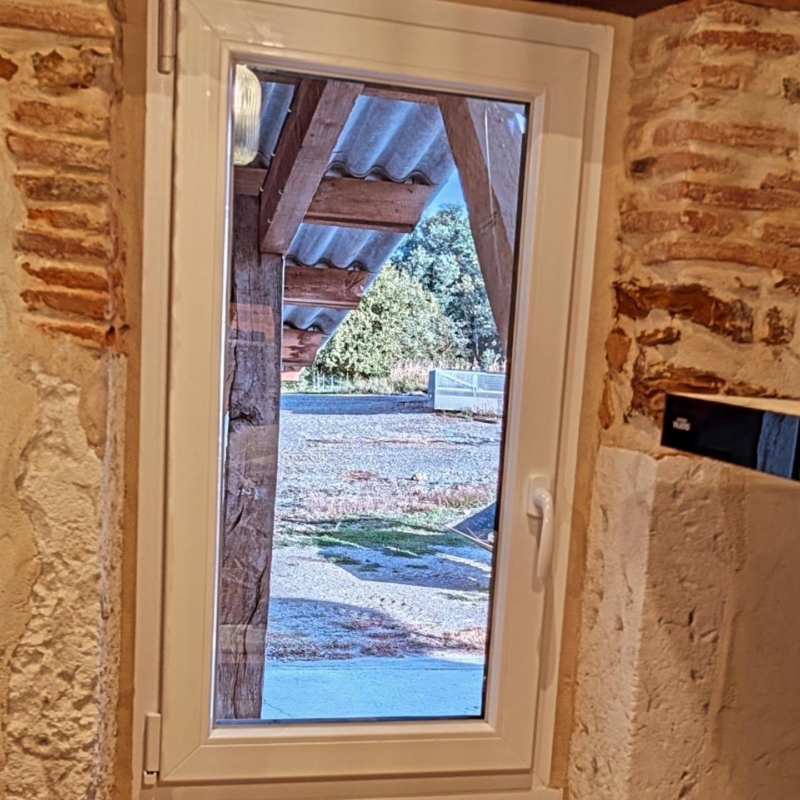 Fenêtre PVC blanche encadrée de pierre et de briques apparentes à l'intérieur d'une maison ancienne à Misson