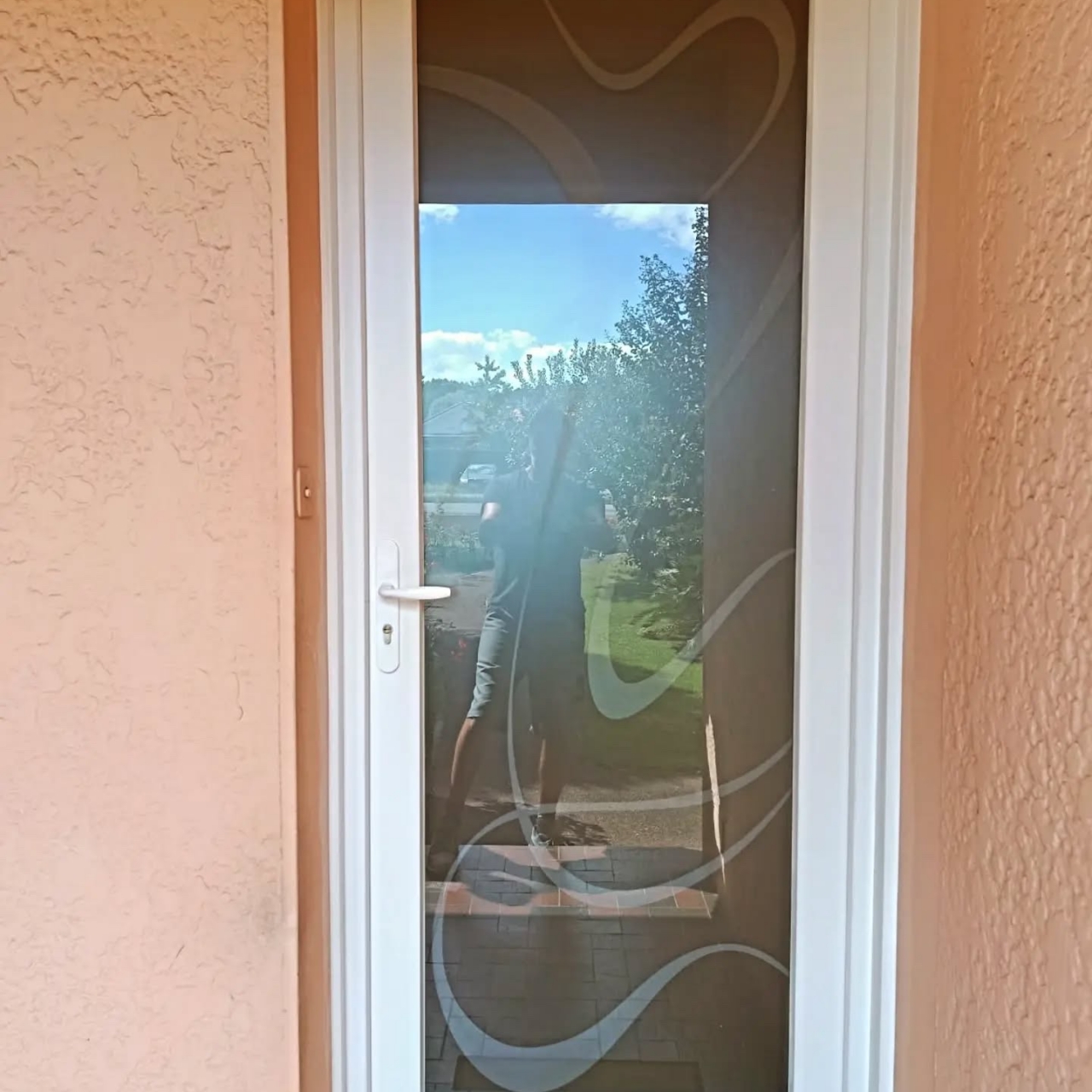 Porte d'entrée PVC blanche OuvertureS Nacre très vitrée, vitrage dépoli à motifs gravés, vue côté rue sur une façade enduite à Soustons
