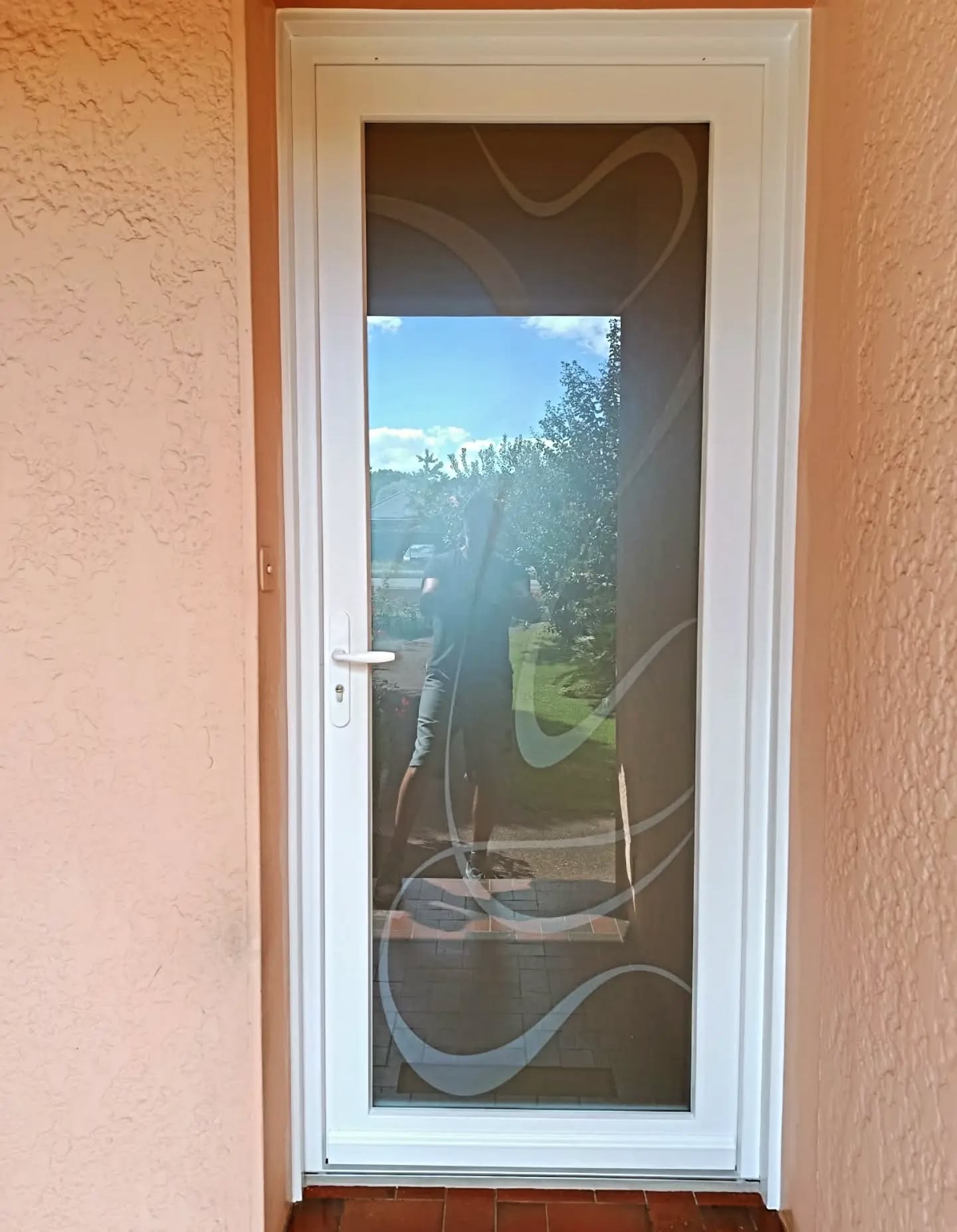 Porte d'entrée PVC blanche OuvertureS Nacre très vitrée, vitrage dépoli à motifs gravés, vue côté rue sur une façade enduite à Soustons