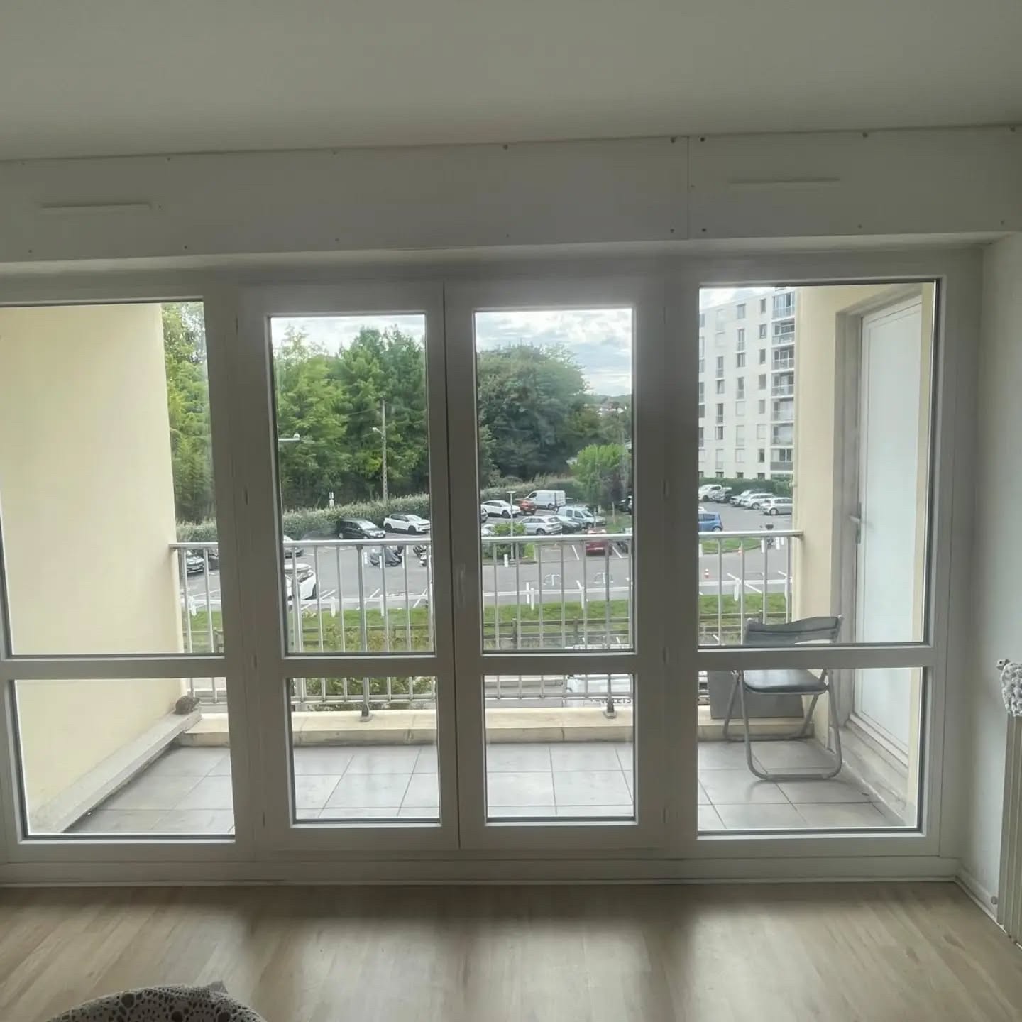 Vue intérieure d'une porte-fenêtre PVC blanche à deux vantaux entre deux châssis fixes, ouvrant sur un balcon à Anglet