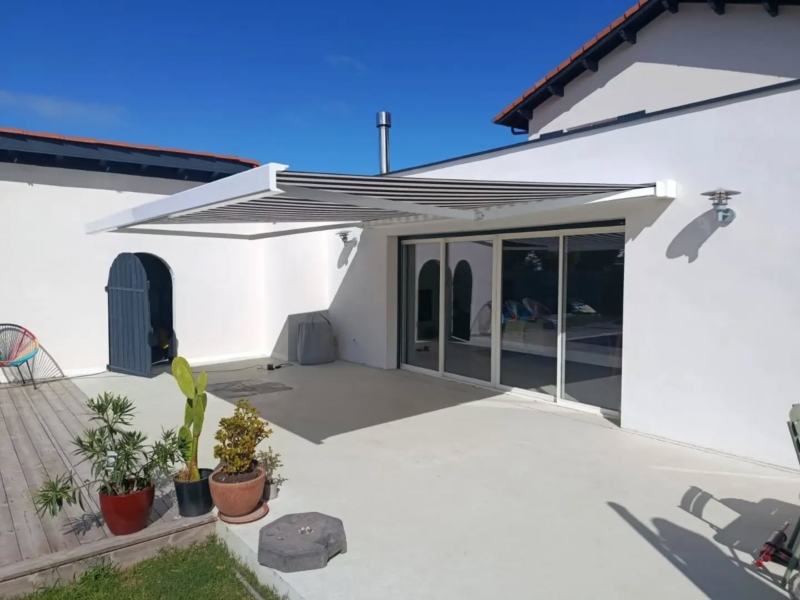 Store banne à toile rayée gris et blanc devant la baie vitrée coulissante d'une maison blanche à Soustons