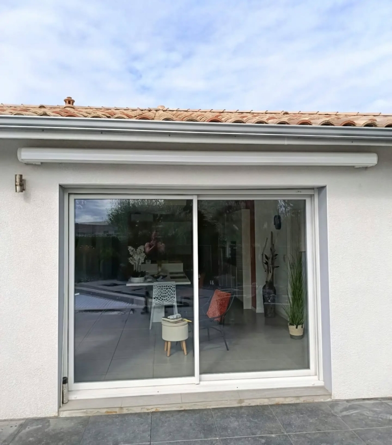 Coffre blanc du store banne rétracté sous la gouttière, au-dessus d'une baie coulissante, maison à Soustons