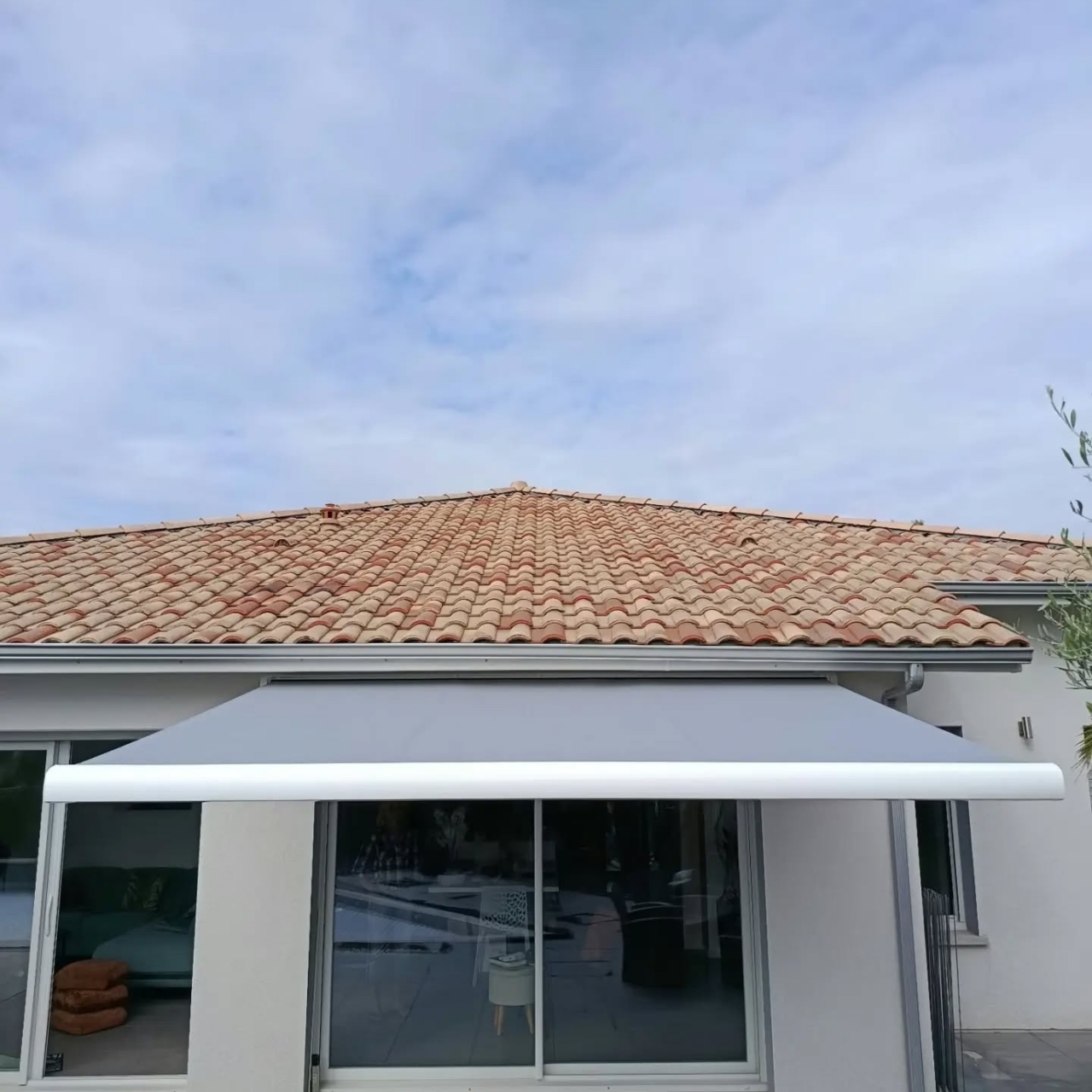 Façade d'une maison avec un store coffre déployé devant les baies coulissantes, toile grise et barre de charge blanche, à Soustons