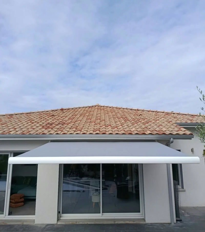 Façade d'une maison avec un store coffre déployé devant les baies coulissantes, toile grise et barre de charge blanche, à Soustons