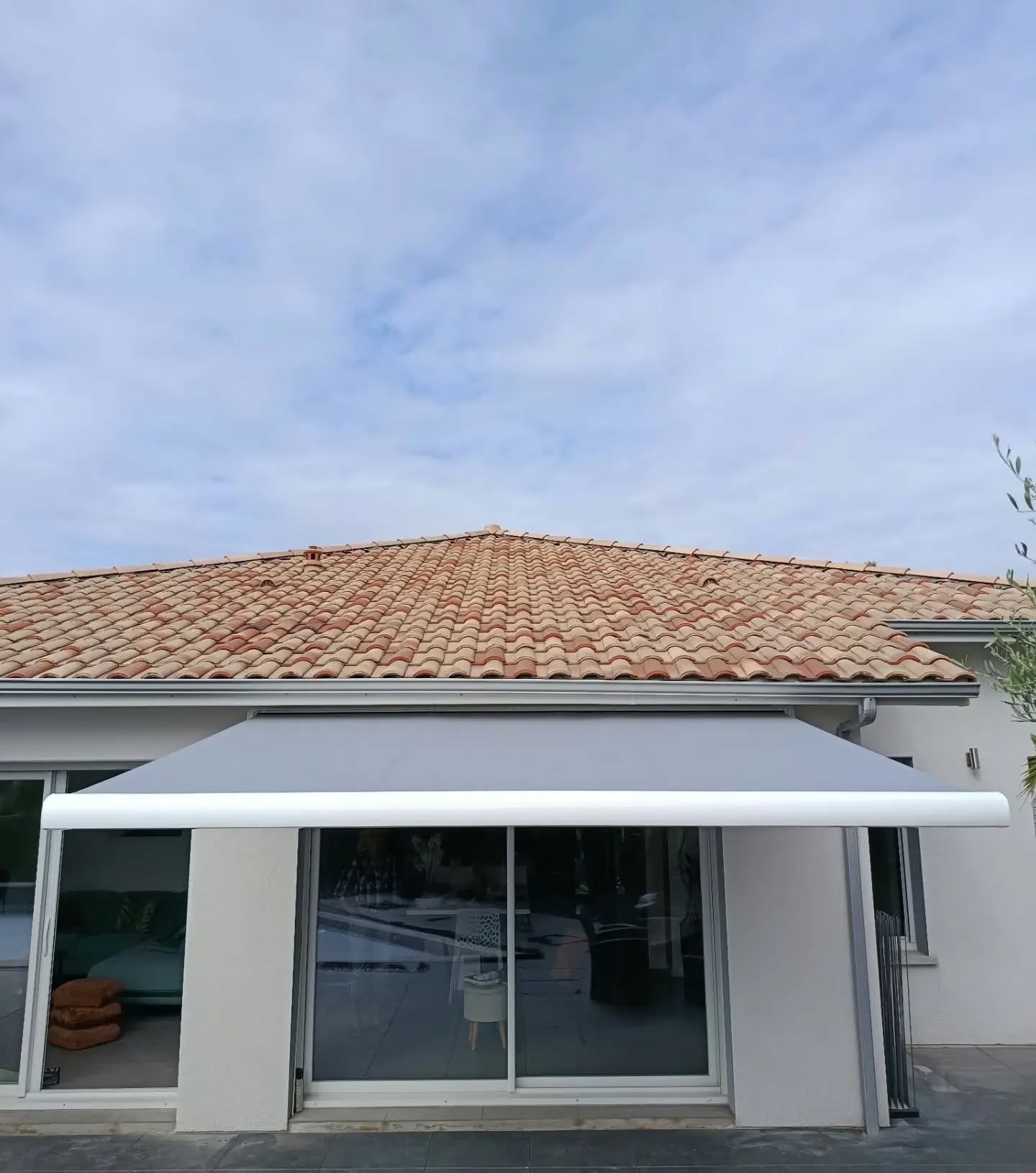 Façade d'une maison avec un store coffre déployé devant les baies coulissantes, toile grise et barre de charge blanche, à Soustons