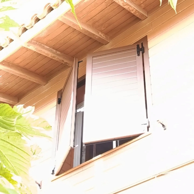 Volet battant aluminium ouvert sous la charpente apparente d'une maison à bardage bois à Vieux-Boucau